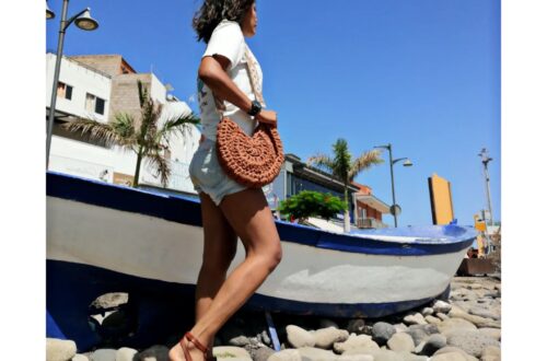 Mujer posando con un bolso de ganchillo marrÃ³n junto a un bote de remos.